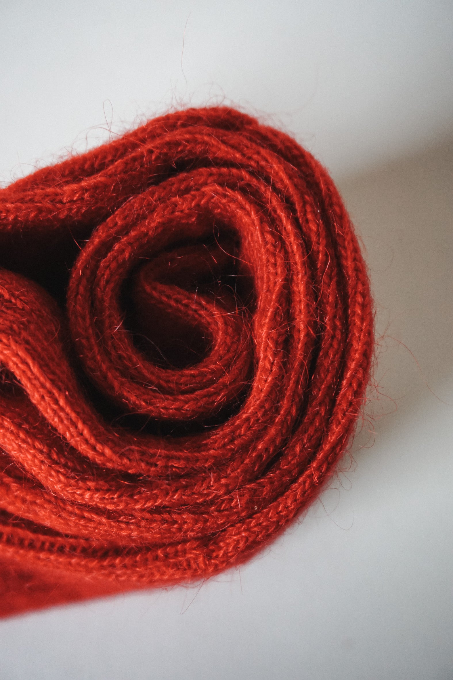 Women’s mohair calf length red socks with ribbed cuff and soft knit texture for comfort when worn with leather boots. Close up view of socks rolled up.